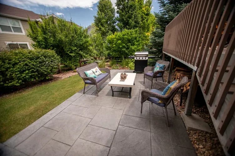 Stamped concrete patio with outdoor dining set, cushions, and shade umbrella on a bright Colorado day.