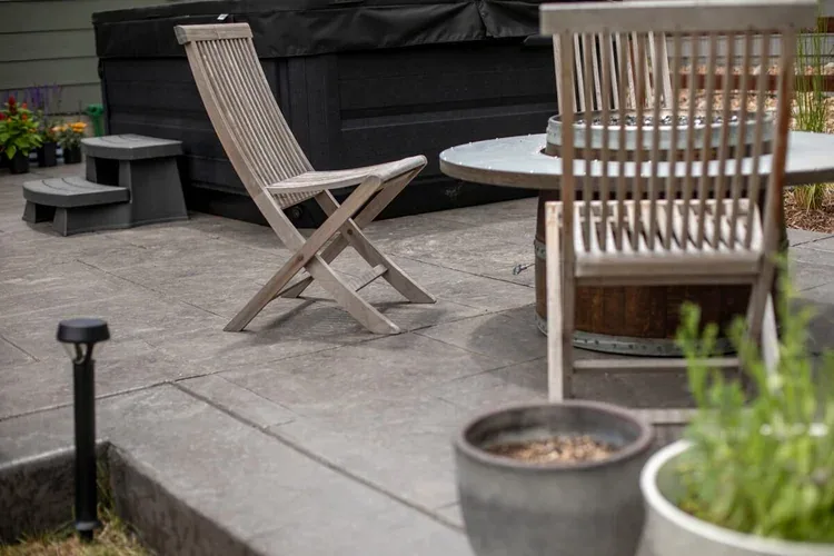 Gas fire pit table with wooden sling chairs on stamped concrete, one of the backyard gathering zones.
