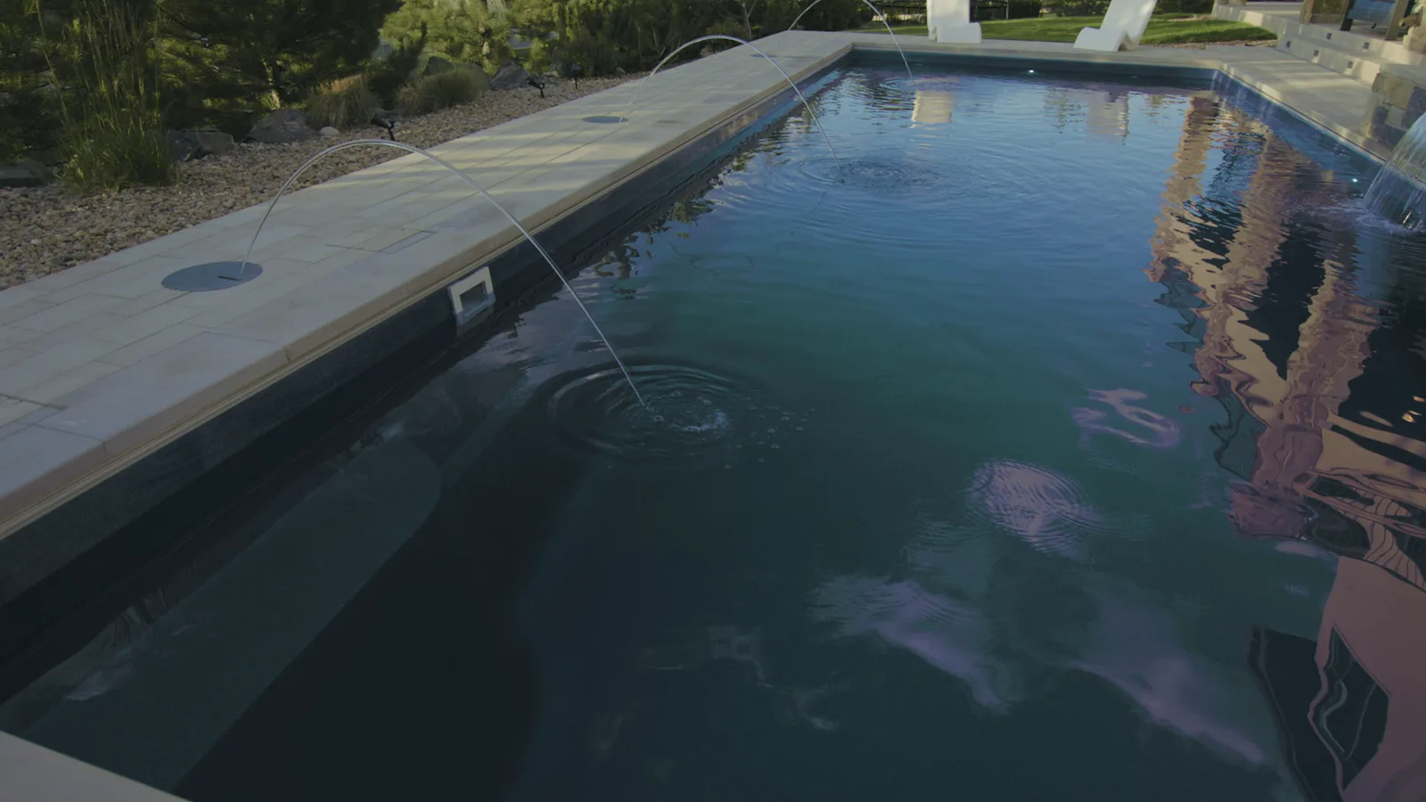 Laminar deck jets arcing over clear pool water with natural-stone coping and a tanning ledge, Zamucen Residence in Colorado.