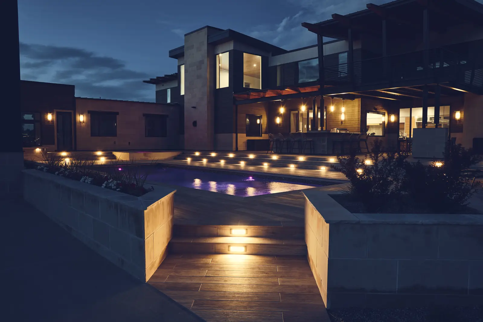 Twilight view of a custom pool, floating deck steps, and landscape lighting at a modern Colorado home