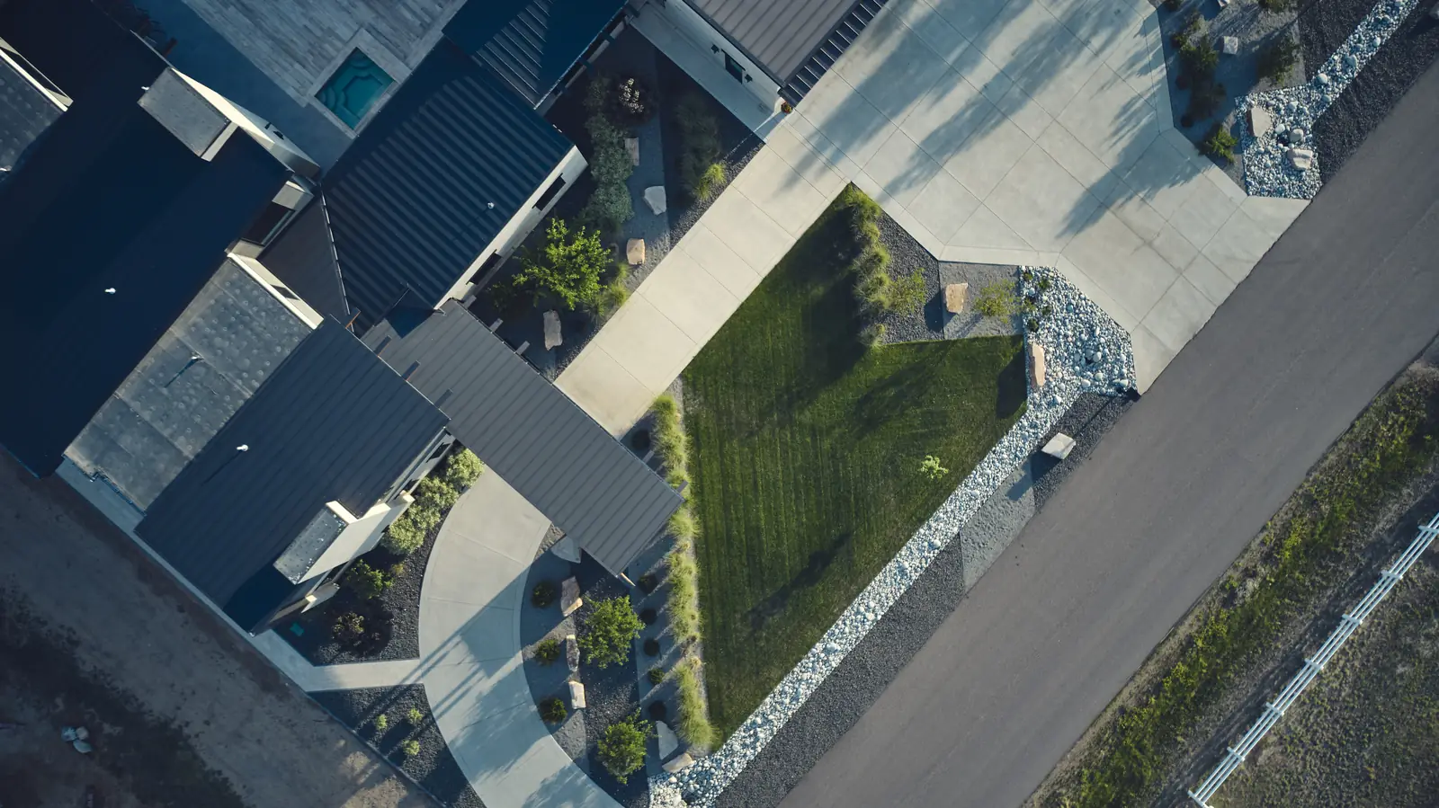 High aerial of a corner-lot modern estate with new landscape, lawn, and drive