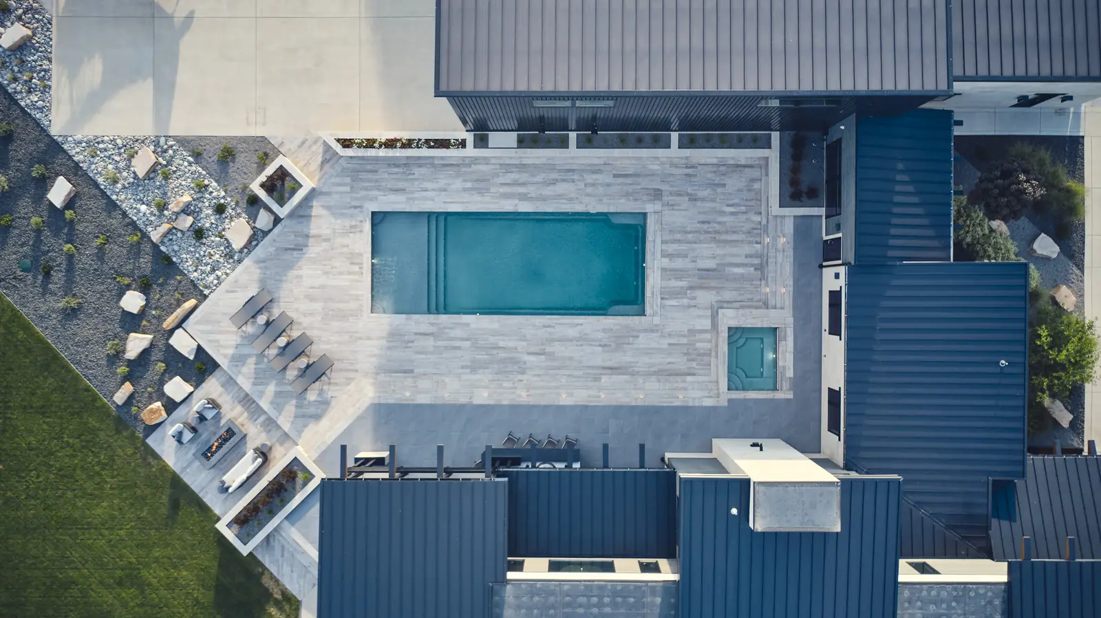 Overhead aerial of pool, spa, and paver surround tucked between dark metal roofs