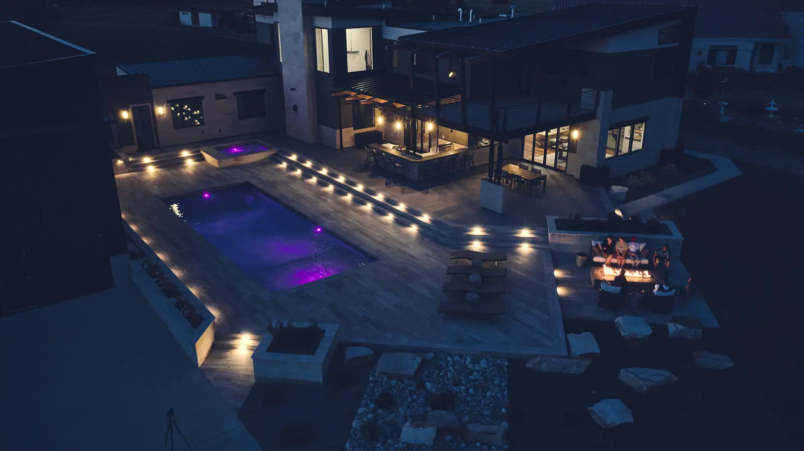 Evening view over an LED-lit custom pool with deck step lighting and a fire pit lounge in Colorado