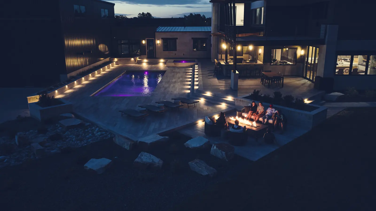 Wide dusk view of the pool, modern home, and fire pit lounge under a fading sky