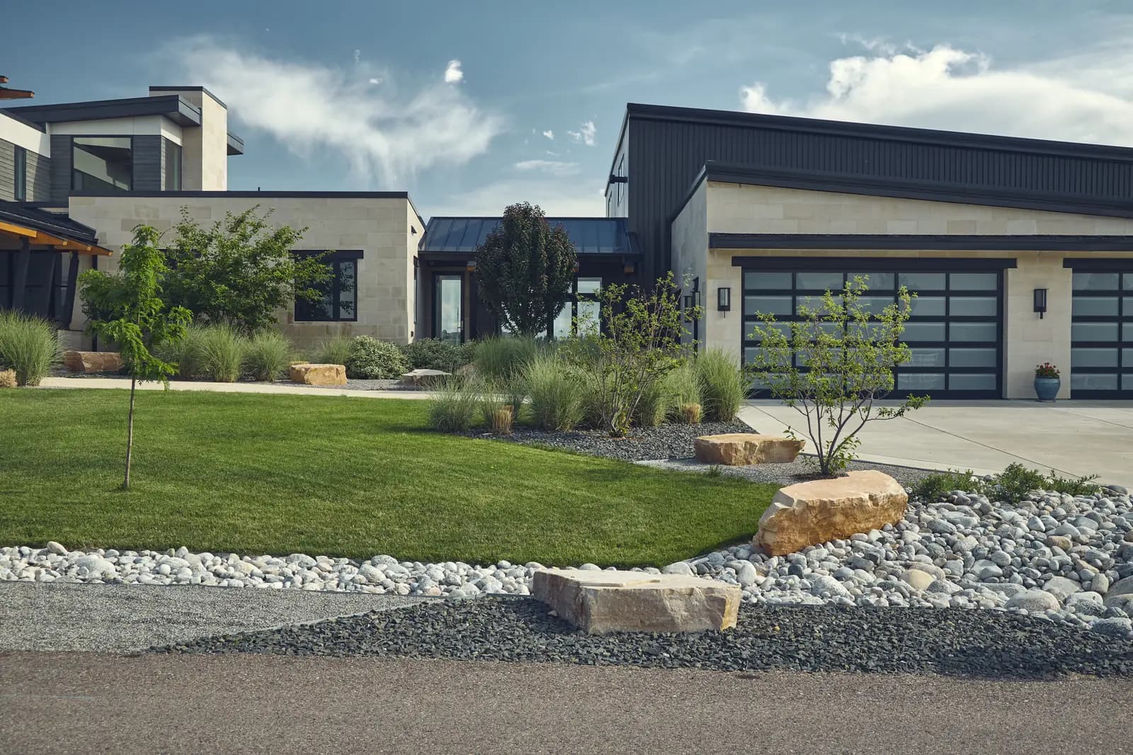 Front entry lawn with boulder and river rock edging beside a modern garage court