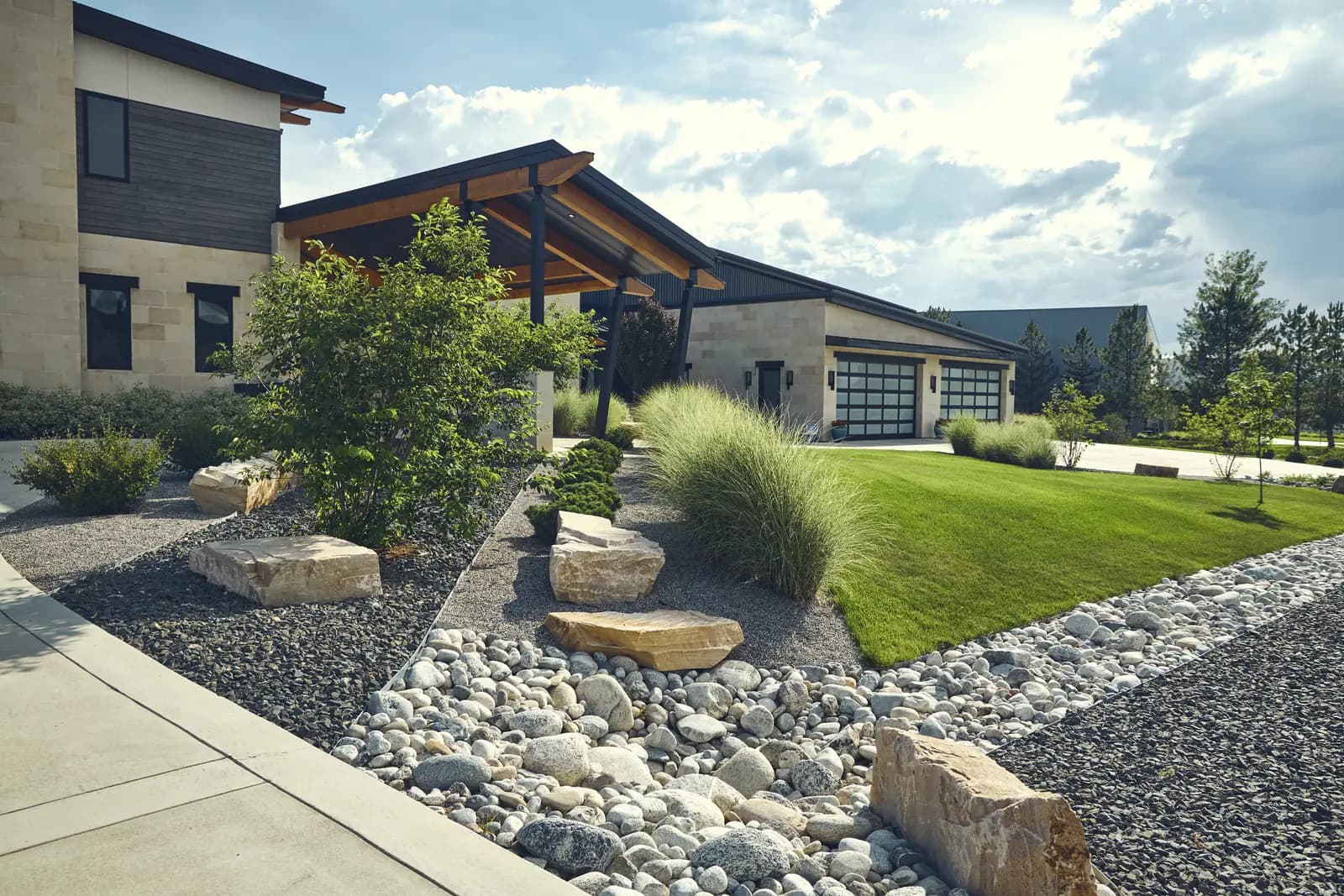 Front walk lined with sandstone boulders, ornamental grasses, and lawn leading to the entry