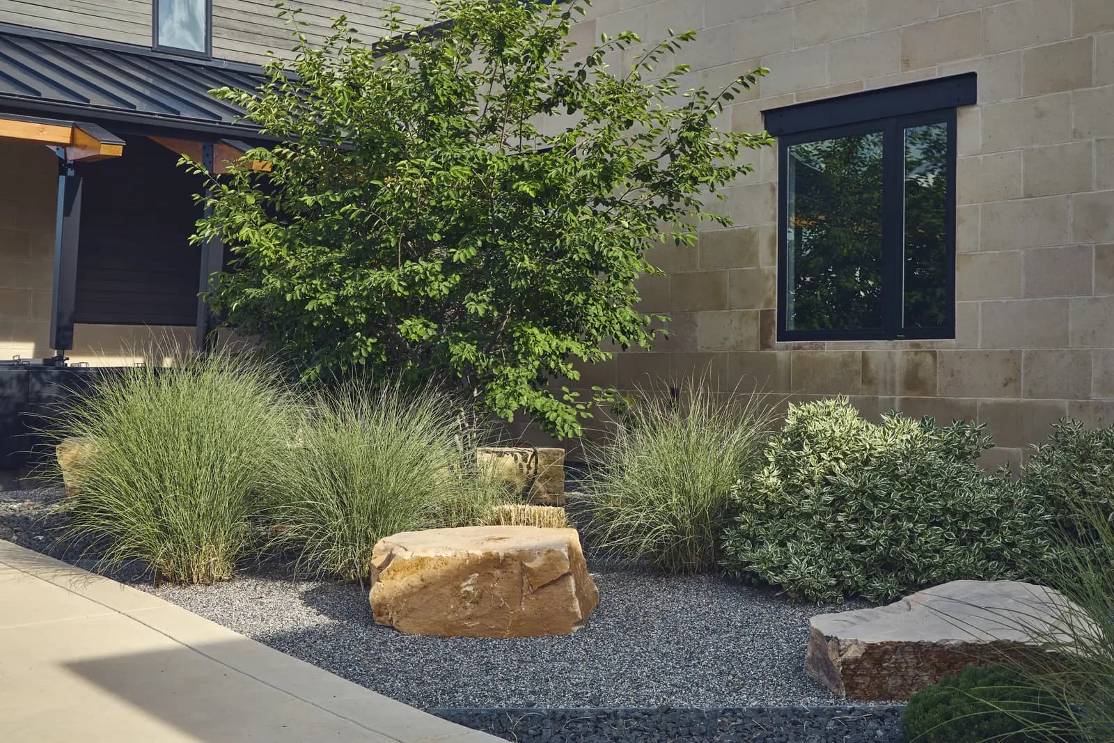 Planting detail of native grasses and sandstone boulders in gravel at the home entry