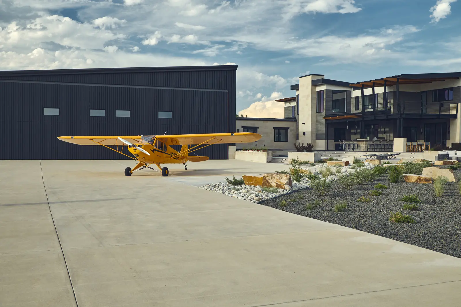 Yellow vintage airplane parked at a black hangar beside the estate landscape