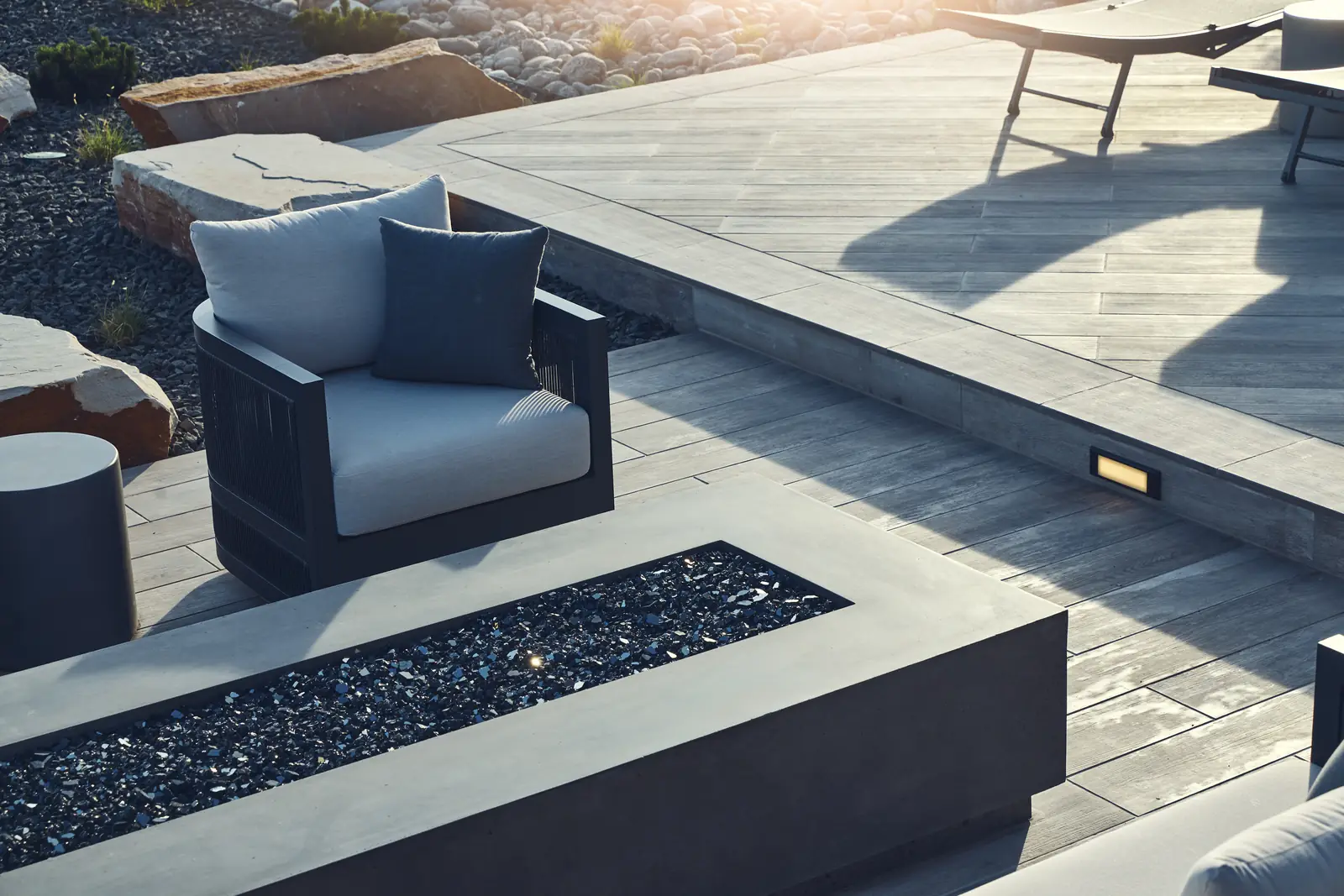 Outdoor armchair beside a linear concrete fire pit filled with black fire glass