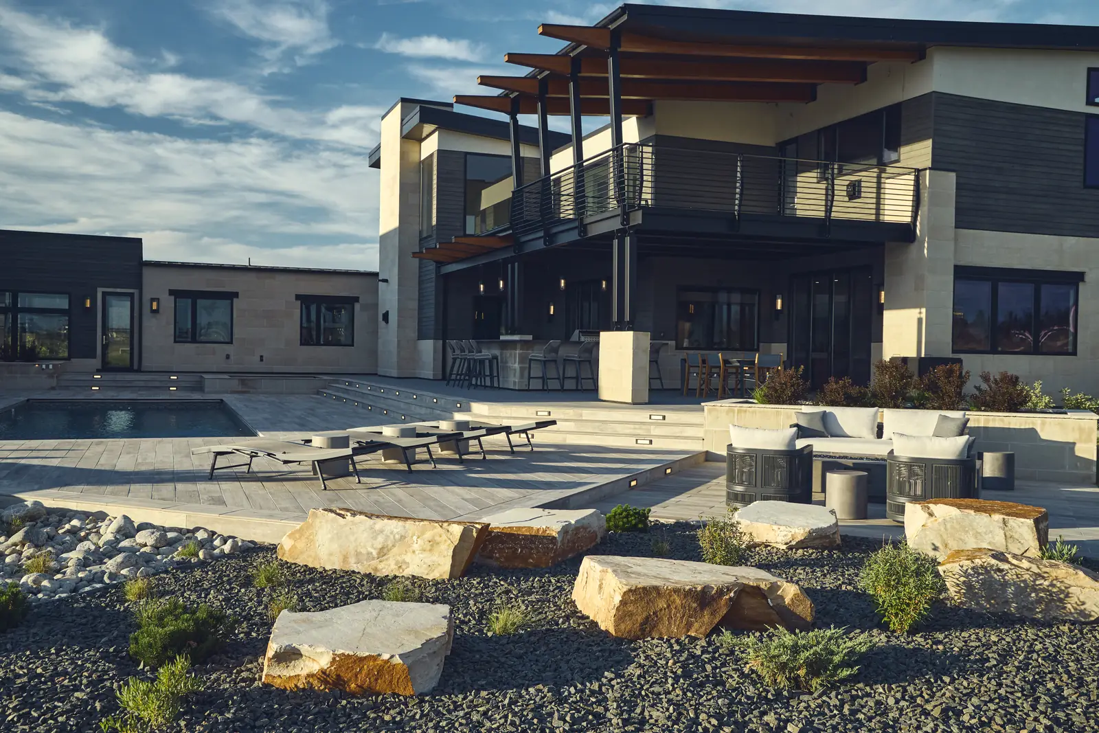 Wide backyard view of the two-story modern home, layered patios, boulder garden, and lounges