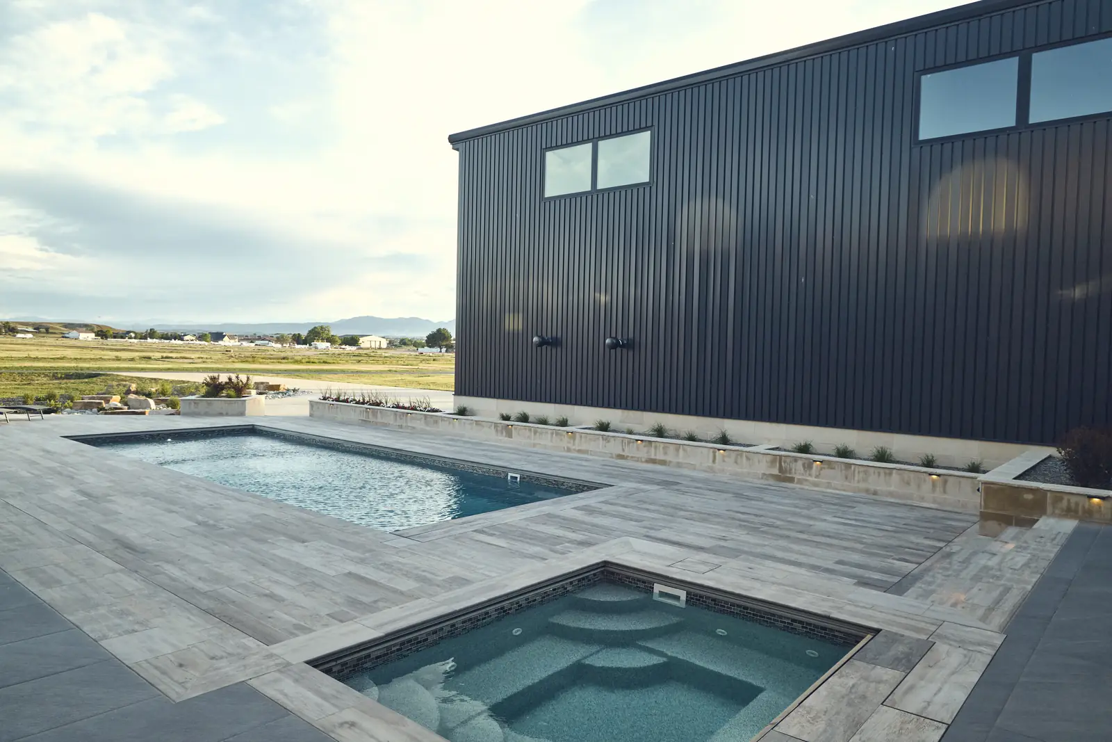 Pool and square spa with corrugated steel hangar wall and open prairie beyond
