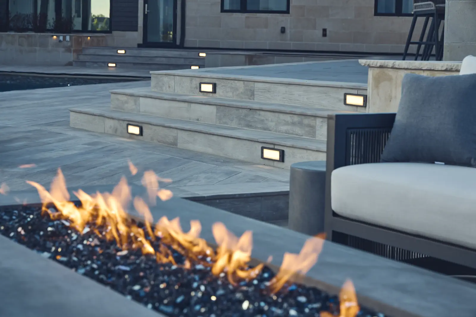 Close-up of fire glass flames with outdoor sofa and limestone steps behind