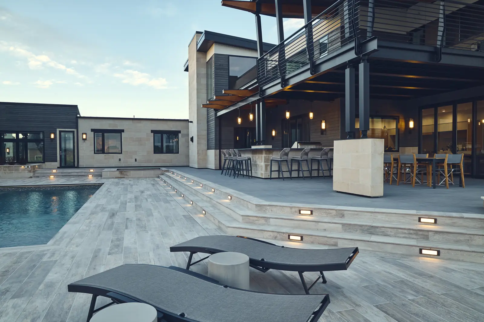 Dusk view of pool steps, chaise lounges, and the balcony of the modern home