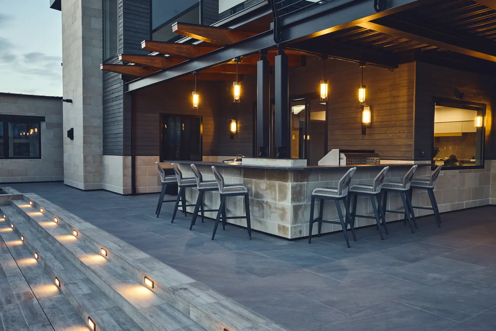 Outdoor bar with pendant lights and stools under the pergola at dusk
