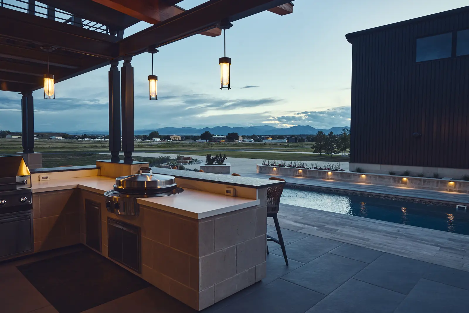 Outdoor kitchen with built-in grill overlooking the pool and prairie sunset