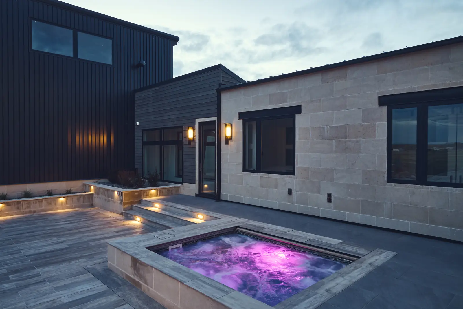 Purple-lit spa beside limestone walls and accent lighting at night