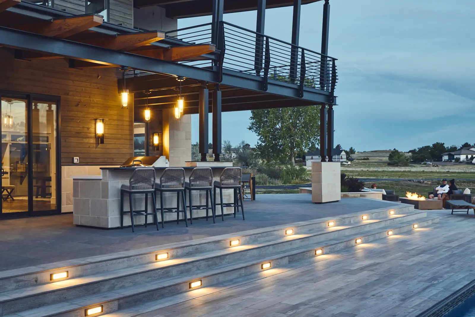 Outdoor kitchen bar and lit pool steps under a covered pergola at dusk