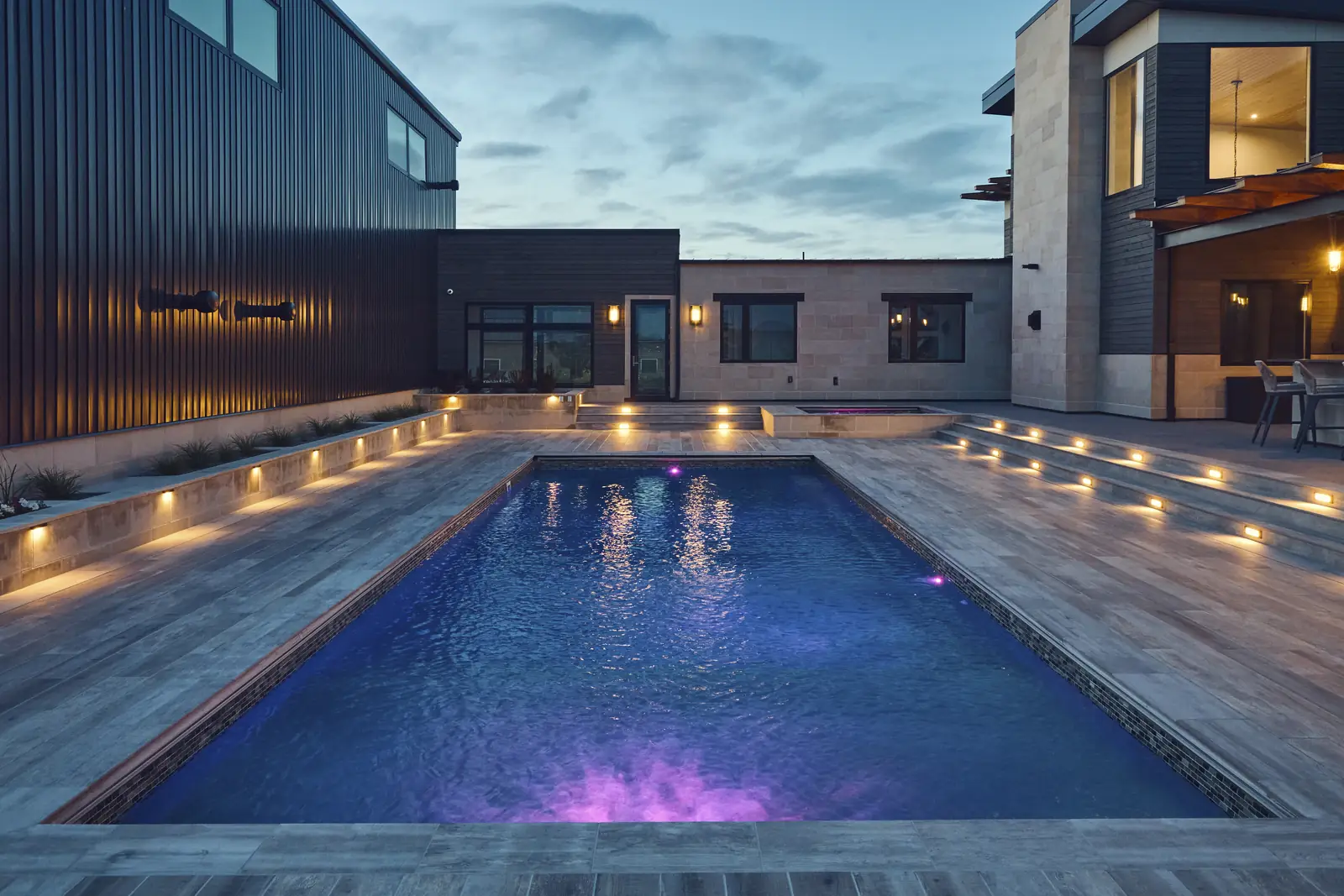 Night pool view toward the lit modern home with step lights along the deck