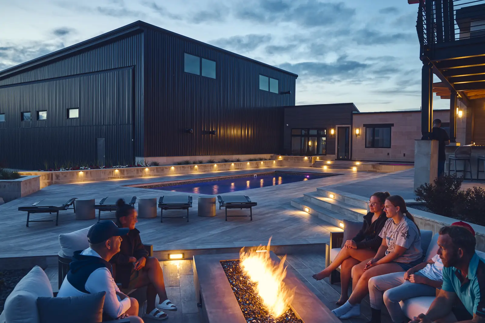 Family gathered around the fire pit beside the lit pool at night